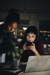 Confident female colleagues using smart phones while working late at coworking space