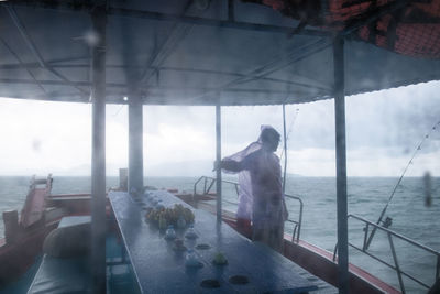 People standing by sea against sky seen through glass window