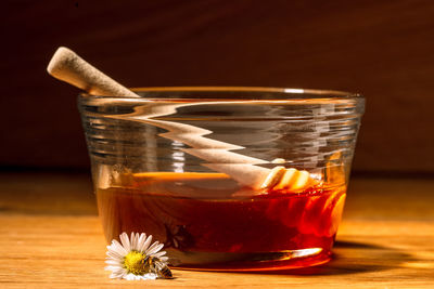 Jar of golden honey with wooden spoon  on wooden table next to white daisy flower with bee on it