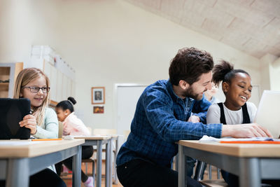 Smiling teacher with students using digital tablet at classroom