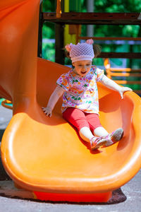 Cheerful cute girl playing on slide at playground