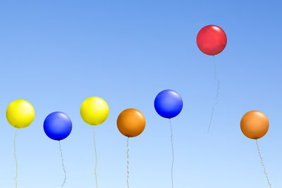 Low angle view of multi colored balloons against blue sky