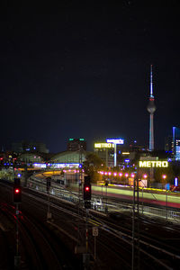 Illuminated railroad tracks amidst buildings in city at night