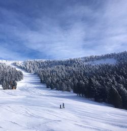 Scenic view of ski pist with two skiing persons against sky