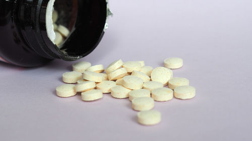 Close-up of pills spilling from bottle against white background