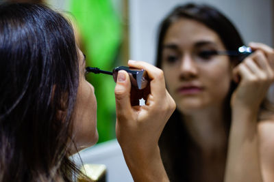 Close-up of woman applying mascara against mirror