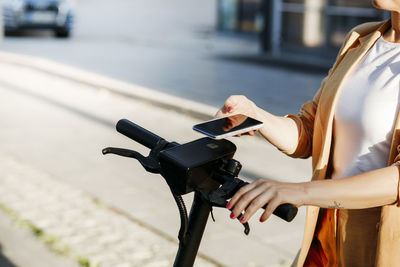 Mature female professional using mobile phone for scanning qr code on electric push scooter