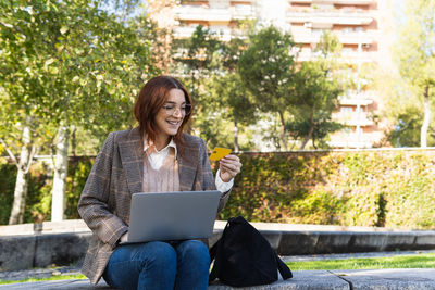 Businesswoman smiling while holding a credit card and using laptop for online shopping.