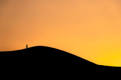 Silhouette person on landscape against sky during sunset