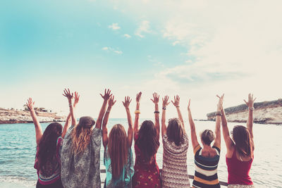 Rear view of female friends with arms raised at beach
