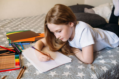 The girl after school plays at home, draws with pencils and felt-tip pens