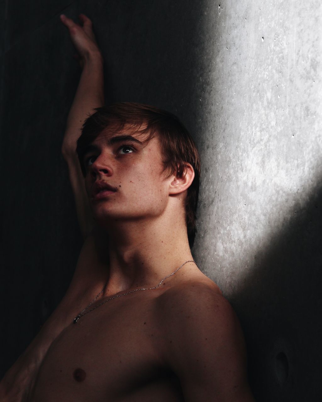 shirtless, indoors, one person, portrait, young adult, real people, lifestyles, front view, headshot, looking at camera, young men, looking, adult, wall - building feature, human body part, standing, studio shot, black background, arms raised, chest, contemplation