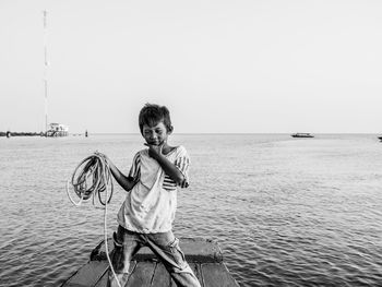 Boy holding rope while standing on pier in sea