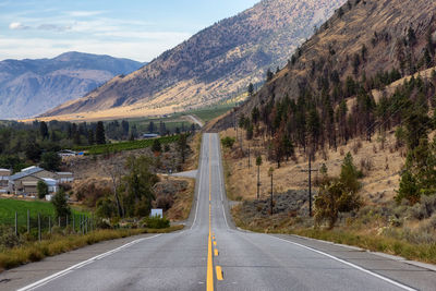 Country road leading towards mountains against sky