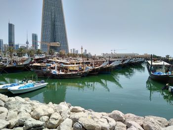 Boats moored at harbor by buildings against clear sky