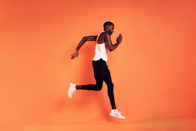 Side view of man running against orange background