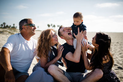 Baby smashing dad in face, sitting on beach with family smiling