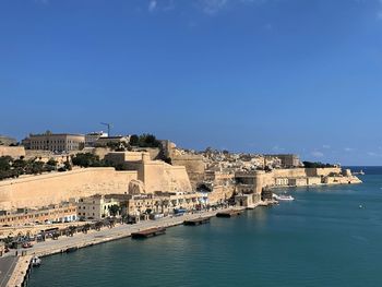 Buildings by sea against clear blue sky