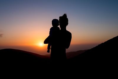 Silhouette man standing on mountain against clear sky during sunset