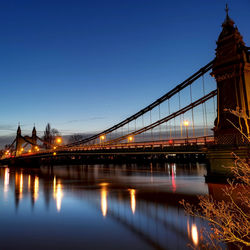 Illuminated bridge over river with city in background