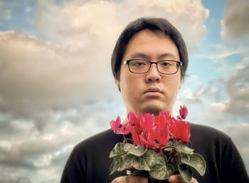 Portrait of man wearing red flower against sky