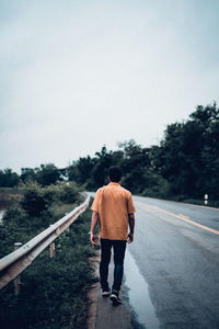 Rear view of man walking on road against sky