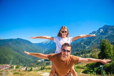 Smiling young woman with arms outstretched against mountain range