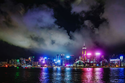 Illuminated buildings by river against sky at night