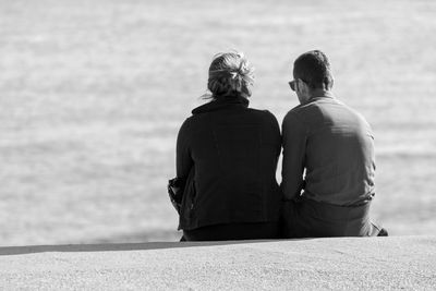 Rear view of couple sitting on sand at beach