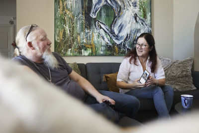 Mature couple sitting on sofa, woman showing cell phone