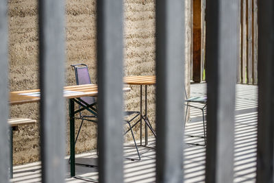 Empty chairs with table at sidewalk cafe seen through fence
