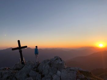 Man standing on rock against sky during sunset
