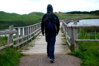 Rear view of man walking on footbridge over river by green hills