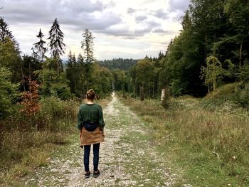 Rear view of woman walking in forest against sky
