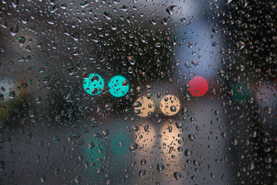 Full frame shot of raindrops on glass with cars and traffic light in background 