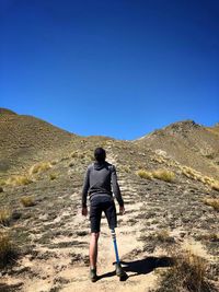 Rear view of disable man standing on mountain against clear blue sky