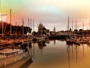 Sailboats moored in river against cloudy sky during sunset