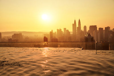 Infinity pool against buildings in city during sunset