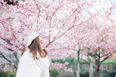 Low angle view of woman standing by pink cherry blossom tree
