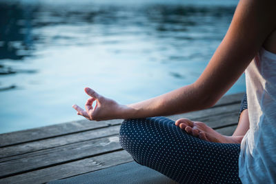 Low section of woman practicing yoga on pier over lake