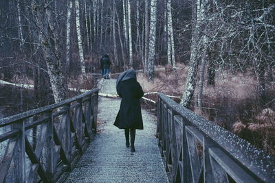 Rear view of woman walking on footbridge during winter