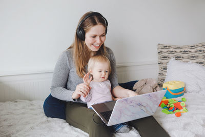 Smiling young woman with daughter sitting against wall