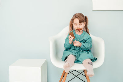 Girl sitting on chair against wall at home