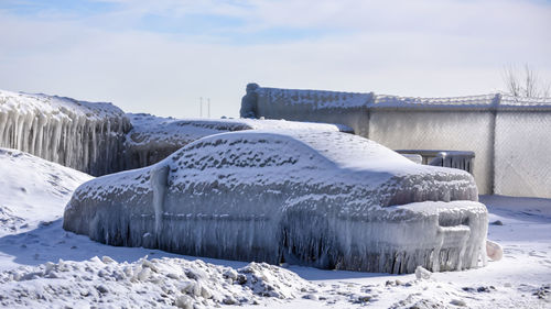 Frozen car on snow covered field against cloudy sky