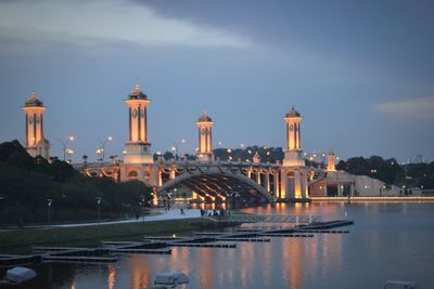 Illuminated buildings by river against sky in city