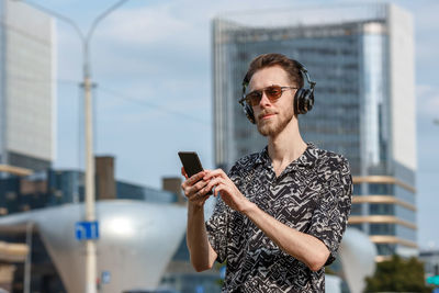 A young man with a smartphone in headphones and sunglasses listens to music