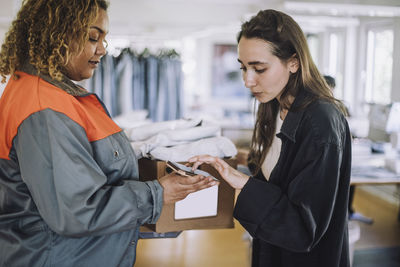 Female fashion designer receiving package from delivery person at workshop