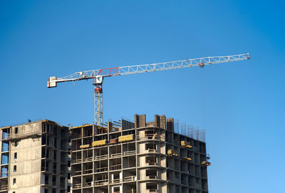 Low angle view of crane against clear blue sky