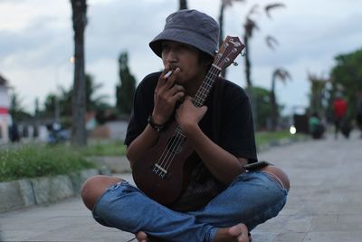 Full length of man holding guitar smoking while sitting on road