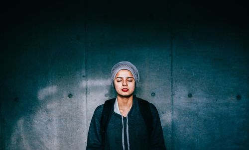 Portrait of young woman standing by wall